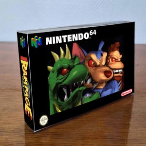 以下が含まれることがあります： Rampage World TourのNintendo 64ビデオゲームボックス。黒い箱にはN64のロゴ、黄色と赤の文字でRampage World Tourのタイトル、そして緑のトカゲ、青いオオカミ、茶色のサルの3体のモンスターのグラフィックが描かれています。