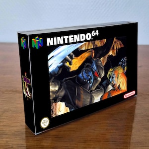 Peut inclure: Une boîte de jeu vidéo Nintendo 64 avec un fond noir et le logo NINTENDO 64 en haut. L'illustration centrale représente un personnage sombre et blindé aux yeux rouges ainsi qu'une silhouette blonde. Un sceau Nintendo est visible en bas.