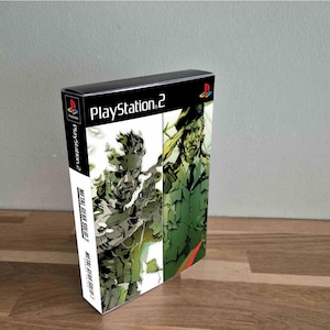 Op de afbeelding: PlayStation 2 game case voor Metal Gear Solid 2. De case heeft een zwarte bovenkant en een kleurrijke illustratie van personages in tinten groen, wit en zwart. Het PlayStation 2-logo is zichtbaar.