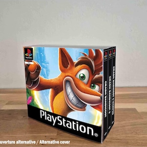 Può includere: Una collezione di tre custodie per videogiochi PlayStation con Crash Bandicoot sulla copertina. I dorsi riportano le scritte Crash Bandicoot, Crash Bandicoot 2 e Crash Bandicoot 3 Warped. Il logo PlayStation è visibile nell'angolo in alto.