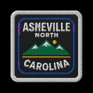 Könnte beinhalten: Gestickter Aufnäher mit dem Text "Asheville North Carolina" in Weiß, über und unter einer Berg- und Sonnengrafik. Der Aufnäher hat einen schwarzen Hintergrund, einen blauen Rand und einen weißen Nahtrand.