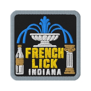 Puede incluir: Un parche bordado cuadrado con borde gris sobre fondo negro. Presenta una fuente blanca con agua azul, una botella de vidrio y una columna clásica. El texto dice FRENCH LICK en amarillo e INDIANA en color blanco bordado.