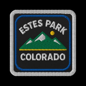 May include: Embroidered patch featuring the text "ESTES PARK COLORADO" in white, arched above a green mountain range with a yellow sun. The patch has a black background with a blue border.