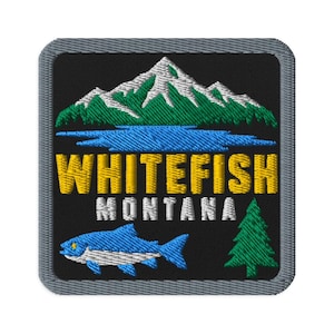 May include: A square embroidered patch with a black background and a gray border. It features a white and green mountain range above a blue lake. The text WHITEFISH MONTANA is embroidered in yellow and white, with a blue fish and a green pine tree.