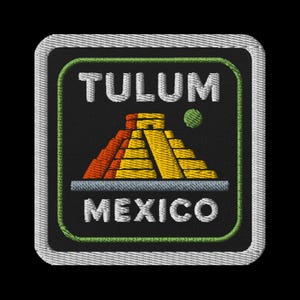May include: Embroidered patch featuring the text "TULUM MEXICO" above and below a colorful illustration of a pyramid. The pyramid is depicted in shades of orange, yellow, and gray, with a green dot to the right.