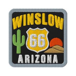 Puede incluir: Un parche bordado cuadrado con fondo negro y borde gris claro. Presenta el texto amarillo WINSLOW, un cactus verde, un escudo amarillo y blanco de la Ruta 66 con el número 66, un sol naranja, colinas de color tostado y el texto blanco ARIZONA.