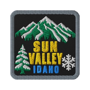 May include: A square embroidered patch with a black background and a gray border. It features a green and white mountain range, a green and white pine tree, a white snowflake, and the yellow and blue text SUN VALLEY IDAHO.