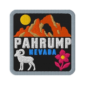 Può includere: Una toppa ricamata quadrata con sfondo nero che raffigura una catena montuosa arancione sotto un sole giallo. Il testo PAHRUMP è in bianco, NEVADA è in blu. Un bighorn bianco si trova a sinistra e un fiore rosa è sulla destra.