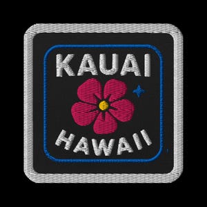 May include: Embroidered patch featuring the words "KAUAI HAWAII" in white, with a pink flower and blue star on a black background. The patch has a blue border and a white stitched edge.