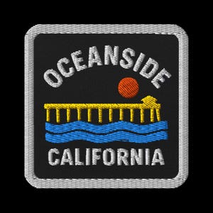 May include: Embroidered patch featuring the text "OCEANSIDE CALIFORNIA" in white, arched above a yellow pier, an orange sun, and blue waves. The patch has a black background and a white border.