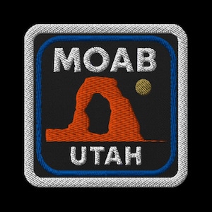 Puede incluir: Parche bordado con el texto "MOAB UTAH" en blanco, un diseño de arco naranja y un punto amarillo sobre fondo negro. Tiene un borde azul y un borde cosido blanco.
