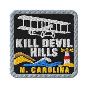 May include: A square embroidered patch with a light grey border on a black background. It features a white biplane, the text KILL DEVIL HILLS in white, a lighthouse, sand dunes, a blue wave, and the yellow text N. CAROLINA at the bottom.