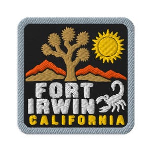 Puede incluir: Un parche bordado cuadrado con borde gris claro sobre fondo negro. Presenta un árbol de Josué color canela, montañas naranjas, un sol amarillo y un escorpión blanco. El texto dice FORT IRWIN en blanco y CALIFORNIA en amarillo.