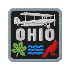 May include: A square embroidered patch with a black background and a light grey border. It features a white biplane above the white text OHIO, with a green buckeye leaf, blue wavy lines, and a red cardinal bird positioned below the text.