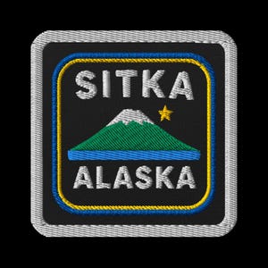 Könnte beinhalten: Gestickter Aufnäher mit dem Text "SITKA ALASKA" und einer Berg- und Stern-Grafik. Das Design zeigt einen blauen See, einen grünen Berg und einen gelben Stern auf schwarzem Hintergrund, umrahmt von einem blau-gelben Rand.