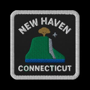 Op de afbeelding: Geborduurde patch met de tekst "NEW HAVEN CONNECTICUT". Het ontwerp toont een groene heuvel met een boom en een blauwe basis op een zwarte achtergrond, omlijst door een witte rand, allemaal gestikt met witte draad.