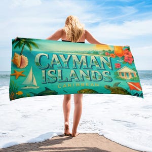 May include: A beach towel featuring a turquoise background with the words "CAYMAN ISLANDS CARIBBEAN" in white. The towel has illustrations of a sailboat, sea life, and tropical flowers. A woman stands on the beach holding the towel.