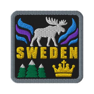 Op de afbeelding: Een vierkante geborduurde patch met een grijze rand op een zwarte achtergrond. Het toont een witte eland, blauwe en paarse abstracte vormen, de gele tekst SWEDEN, drie groene dennenbomen met witte toppen en een gele kroon onderaan.
