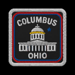 Puede incluir: Parche bordado con la palabra "COLUMBUS" sobre una ilustración de un edificio y "OHIO" debajo. El parche tiene un fondo negro con un borde rojo, azul y blanco. El edificio tiene una cúpula amarilla.