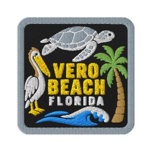May include: A square embroidered patch with a black background and a gray border. It features a gray sea turtle, a white and yellow pelican, a green palm tree, and a blue ocean wave. The text VERO BEACH FLORIDA is embroidered in yellow and white.