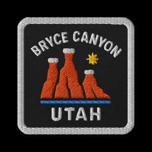 May include: Embroidered patch featuring the words "BRYCE CANYON UTAH" in white, arched above a depiction of orange rock formations with white tops and a yellow star. A blue line runs beneath the formations. The patch has a black background and a white border.