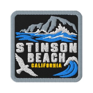 May include: A square embroidered patch with a black background and a grey border. It features a white mountain range above blue ocean waves, a white bird in flight, a blue wave, and the white text STINSON BEACH with yellow text CALIFORNIA.