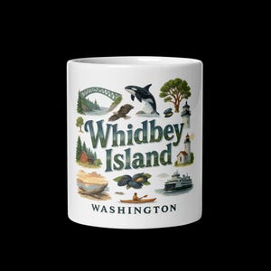 May include: White ceramic mug featuring illustrations of Whidbey Island, Washington. The design includes a bridge, an orca, a lighthouse, and the text "Whidbey Island" in green and blue. The word "Washington" is printed below.