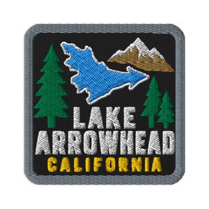 May include: A square embroidered patch with a black background and a gray border. It features a blue lake shape, brown mountains with white peaks, and green pine trees. The text reads LAKE ARROWHEAD in white and CALIFORNIA in yellow.