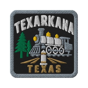 May include: A square embroidered patch with a black background and a gray border. It features a white steam locomotive, two green pine trees, and a gold marker. The text reads TEXARKANA in white at the top and TEXAS in gold at the bottom.