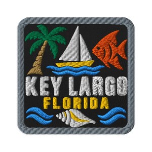 May include: A square embroidered patch with a black background and a gray border. It features a green palm tree, a white sailboat on blue waves, and an orange fish. The text reads KEY LARGO FLORIDA above a white seashell and blue waves.