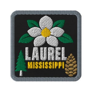 May include: A square embroidered patch with a gray border on a black background. It features a white flower with a yellow center and green leaves, a green pine tree, a brown pinecone, and the text LAUREL MISSISSIPPI in white and yellow.