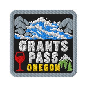 Peut inclure: Un écusson brodé carré avec une bordure grise sur fond noir. Il représente une rivière bleue et blanche, des montagnes grises, un verre à vin rouge et des pins verts. Le texte indique GRANTS PASS en blanc et OREGON en lettres jaunes.