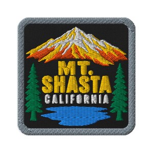 May include: A square embroidered patch with a black background featuring a mountain with yellow and orange peaks, two green pine trees on the sides, and a blue lake at the bottom. The text reads MT. SHASTA CALIFORNIA in yellow and white thread.