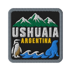 Könnte beinhalten: Ein quadratischer Stickaufnäher mit schwarzem Hintergrund, der grüne und weiße Berge zeigt. Der Text USHUAIA ist in Weiß und ARGENTINA in Gelb gestickt. Darunter befinden sich ein weißer Pinguin und ein blauer Seelöwe bei blauen Wellen.