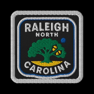 May include: Embroidered patch featuring the words "RALEIGH NORTH CAROLINA" in white, arched over and under a green tree with yellow butterflies. The patch has a black background with a blue border and a gray stitched edge.