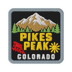 May include: A square embroidered patch with a black background featuring a tan and white mountain peak above a row of green pine trees. The text PIKES PEAK is in yellow, with a red train and yellow sun, and the word COLORADO in white below.