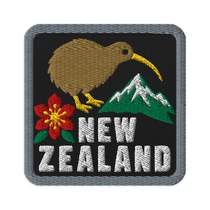 May include: A square embroidered patch with a black background and a gray border. It features a brown kiwi bird with a yellow beak, a green mountain with white snow, a red flower with a yellow center, and the white text NEW ZEALAND.