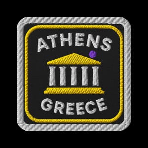 Puede incluir: Parche bordado con las palabras "ATHENS GREECE" en blanco. Presenta una ilustración amarilla y blanca de un edificio con columnas sobre un fondo negro, un borde amarillo y un borde cosido plateado.