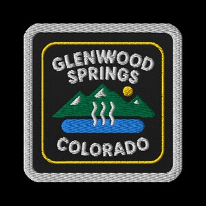 May include: Embroidered patch featuring the words "Glenwood Springs Colorado" in white, with a black background. The design includes green mountains, a blue lake, a yellow sun, and white steam. The patch has a yellow border and a gray stitched edge.