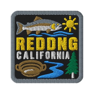 Op de afbeelding: Een vierkante geborduurde patch met een zwarte achtergrond en een grijze rand. Het toont een vis, een gele zon, een blauwe rivier, een bruine goudpan en een groene dennenboom. De tekst luidt REDDING CALIFORNIA in gele en witte hoofdletters.