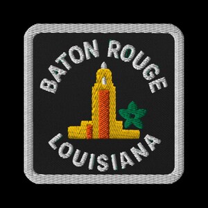 May include: Embroidered patch featuring the words "Baton Rouge Louisiana" in white, arched around a yellow and orange building with a green star. The patch has a black background and a white border.