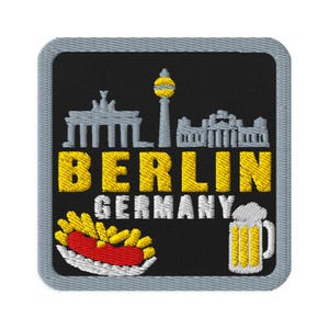 Puede incluir: Un parche bordado cuadrado con fondo negro y borde gris. Presenta una silueta gris de Berlín, el texto amarillo BERLIN, el texto blanco GERMANY, una salchicha roja con patatas fritas amarillas y una jarra de cerveza amarilla con espuma blanca.
