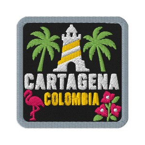 Puede incluir: Un parche bordado cuadrado con fondo negro y borde gris. Presenta un faro blanco y amarillo flanqueado por dos palmeras verdes. Debajo, el texto CARTAGENA COLOMBIA aparece en blanco y amarillo, junto a un flamenco rosa y flores de color rosa.
