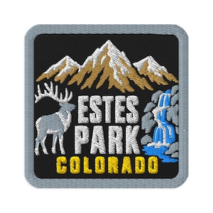 May include: A square embroidered patch with a black background featuring a white elk on the left, a blue waterfall on the right, and brown mountain peaks above. The text ESTES PARK is in white, and the word COLORADO is in yellow at the bottom.