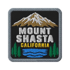 May include: A square embroidered patch with a black background featuring a brown and white mountain peak above the white text MOUNT SHASTA and yellow text CALIFORNIA, with green pine trees and a blue wavy lake at the bottom, all with a grey border.