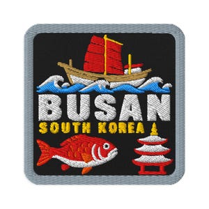 Può includere: Una toppa ricamata quadrata con sfondo nero e bordo grigio. Presenta una giunca con vele rosse su onde blu, il testo bianco BUSAN, il testo giallo SOUTH KOREA, un pesce rosso e una struttura a pagoda rossa e bianca a più livelli.