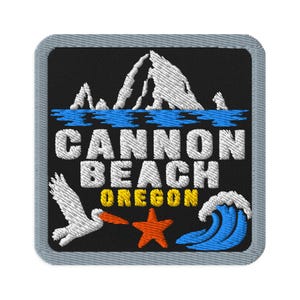 May include: A square embroidered patch with a black background featuring white jagged rock formations above blue water. The text reads CANNON BEACH in white and OREGON in yellow. Below are a white pelican, an orange starfish, and a blue wave.