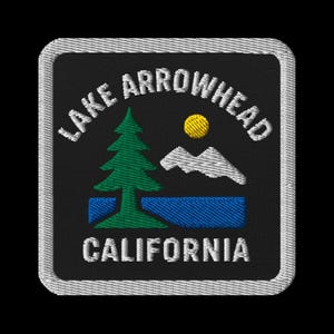 Könnte beinhalten: Gestickter Aufnäher mit dem Text "LAKE ARROWHEAD CALIFORNIA". Das Design zeigt einen grünen Baum, eine gelbe Sonne, weiße Berge und blaues Wasser auf schwarzem Hintergrund, umrahmt von einem weißen Rand. Ideal für Jacken oder Taschen.
