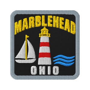 May include: A square embroidered patch with a grey border on a black background. It features the yellow text MARBLEHEAD arched above a white and red lighthouse, a white sailboat with a yellow mast, blue waves, and the white text OHIO below.