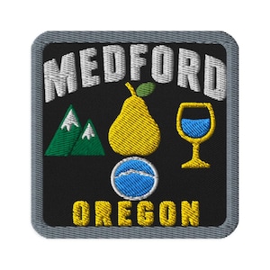 May include: A square embroidered patch with a black background and a gray border. The text MEDFORD is stitched in white at the top, and OREGON is in yellow at the bottom. It features a yellow pear, green mountains, a wine glass, and a blue circle.